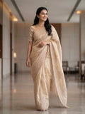 Woman wearing a beige saree with subtle floral embroidery and a matching blouse indoors.