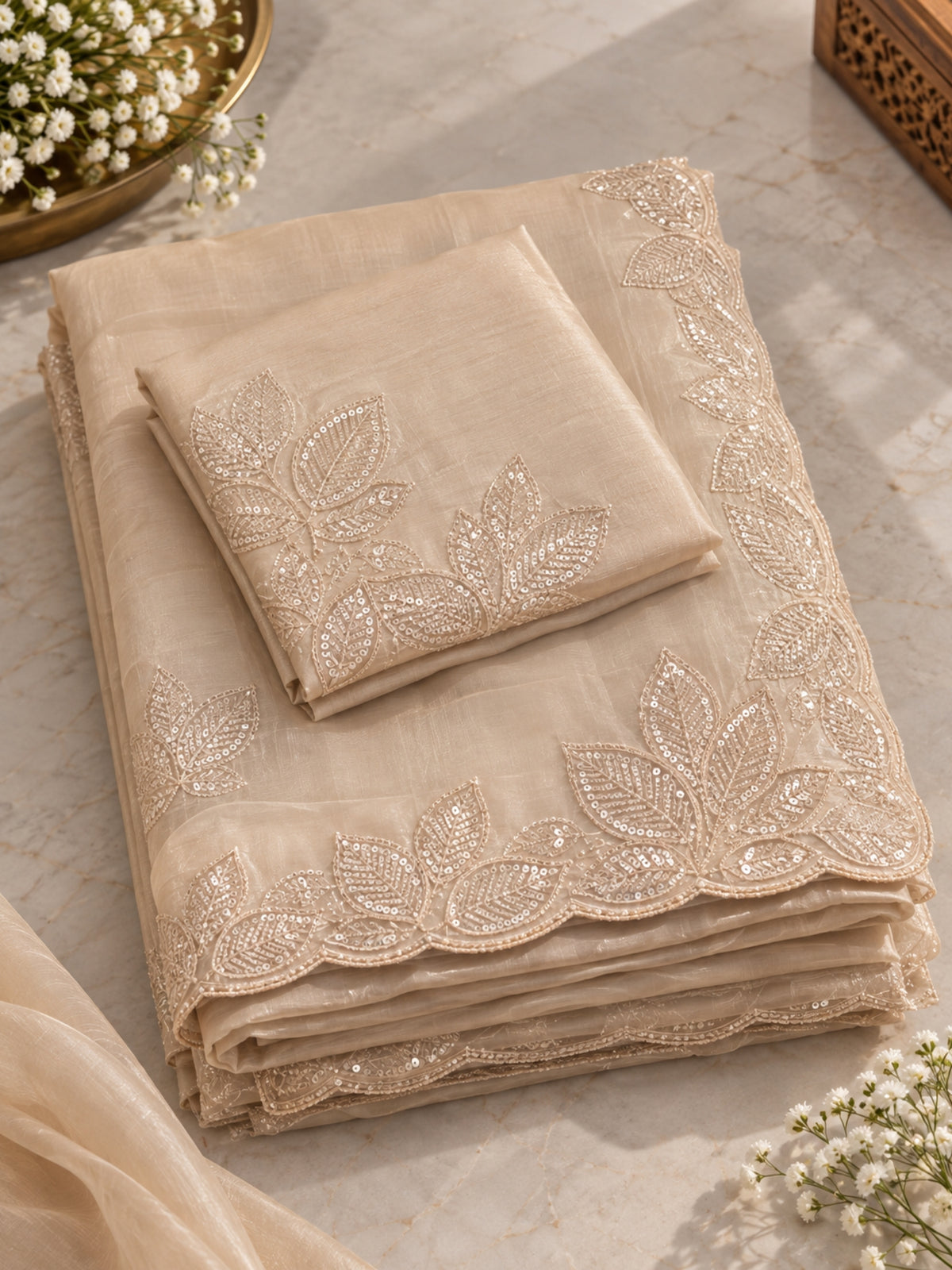 Woman wearing a beige saree with subtle floral embroidery and a matching blouse indoors.