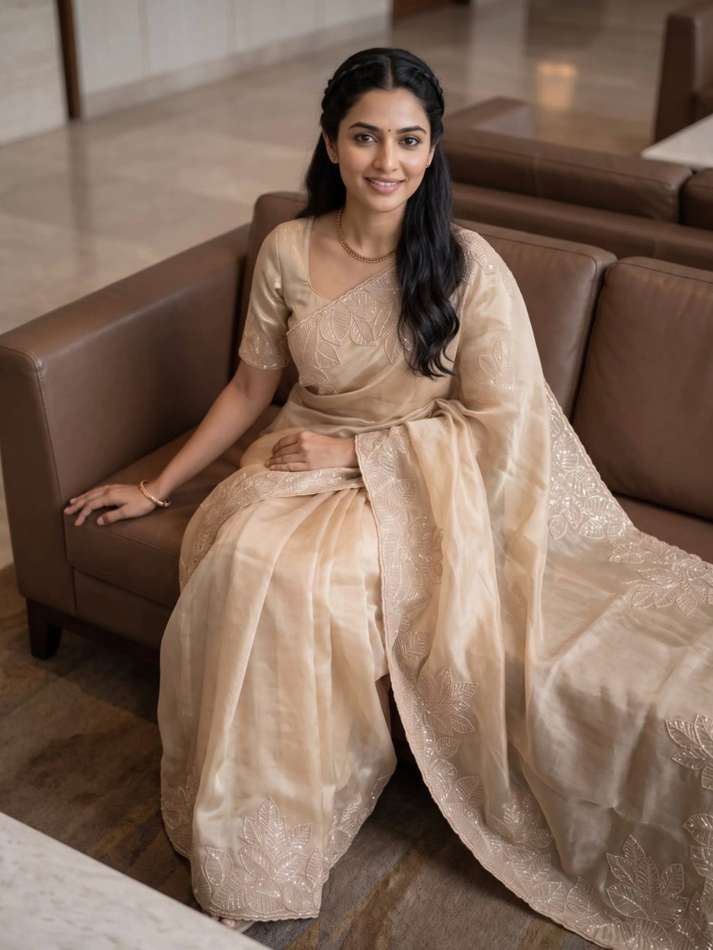 Woman wearing a beige saree with subtle floral embroidery and a matching blouse indoors.
