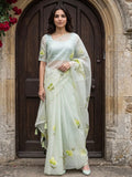 Woman wearing a light green saree with yellow floral prints and tassel detailing outdoors.