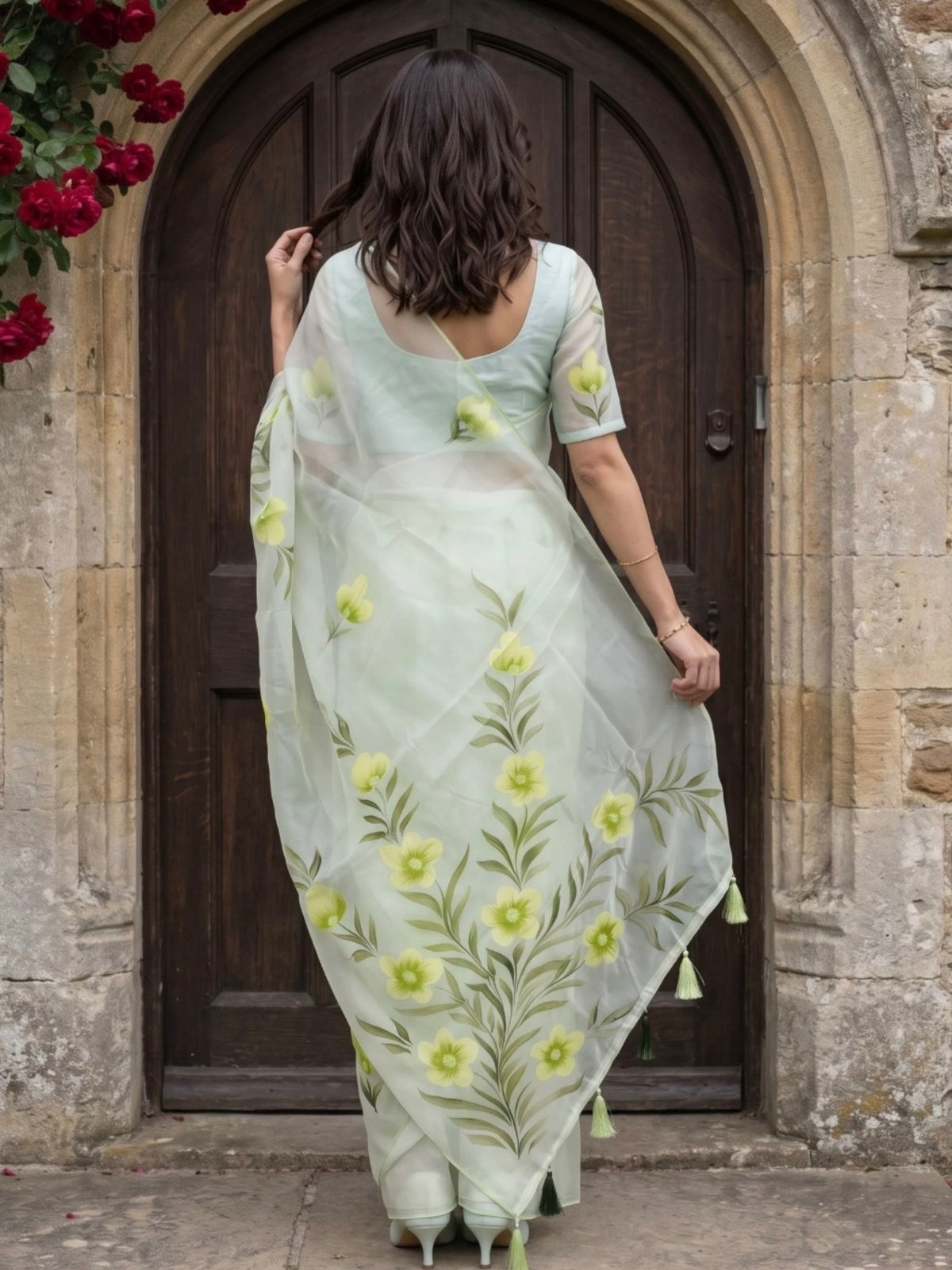 Woman wearing a light green saree with yellow floral prints and tassel detailing outdoors.