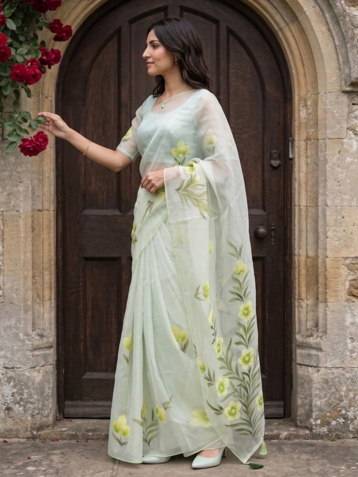 Woman wearing a light green saree with yellow floral prints and tassel detailing outdoors.