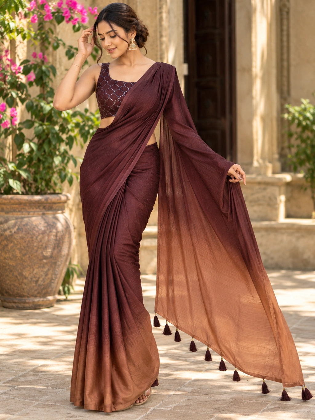 Maroon saree with a sheer pallu and tassel details, draped on a woman in a sunlit courtyard.

