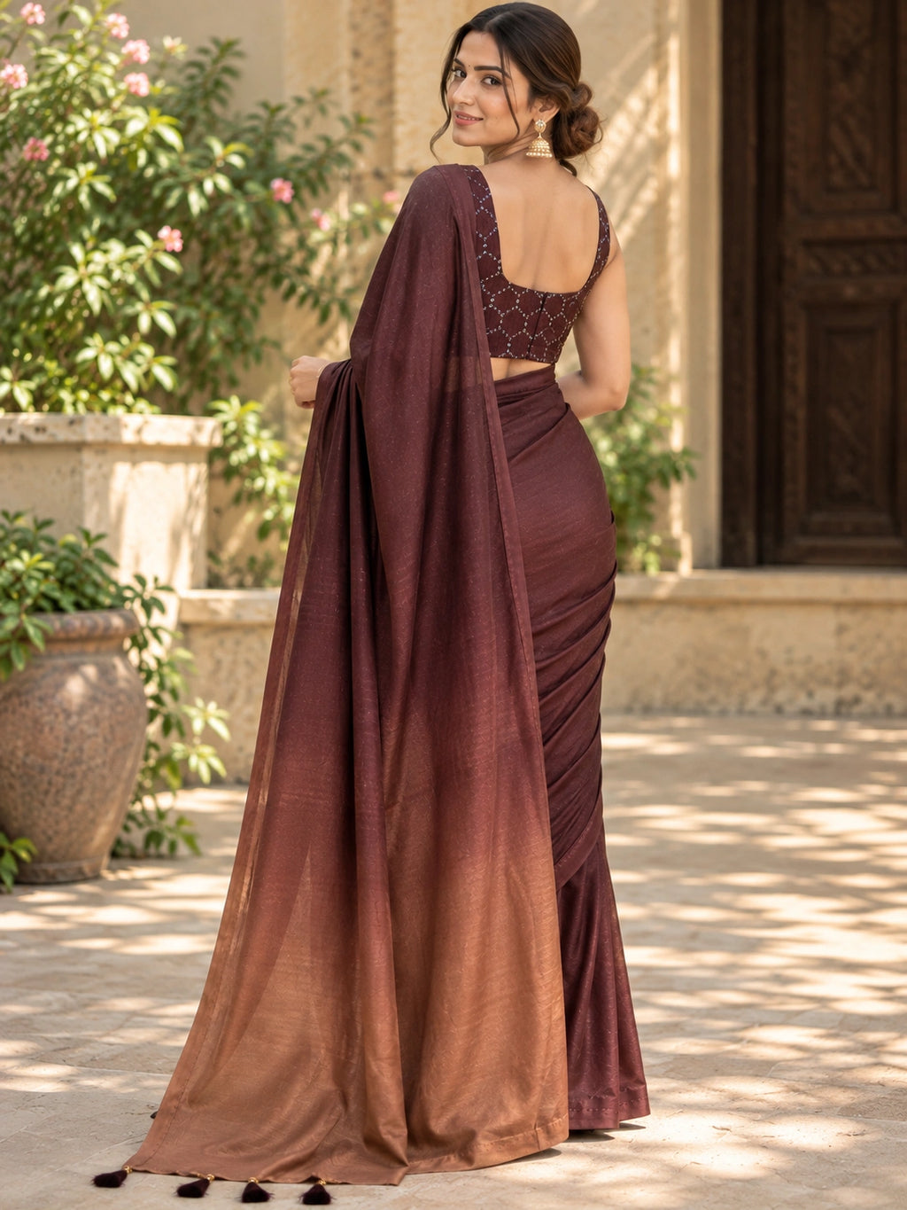 Maroon saree with a sheer pallu and tassel details, draped on a woman in a sunlit courtyard.
