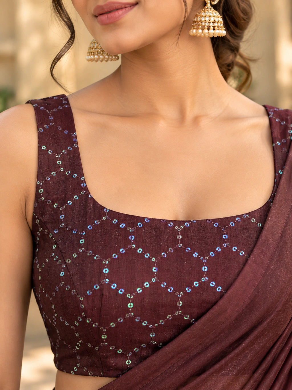 Maroon saree with a sheer pallu and tassel details, draped on a woman in a sunlit courtyard.
