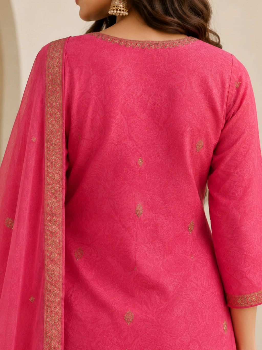 Woman wearing a pink embroidered suit with matching pants and a sheer dupatta indoors.