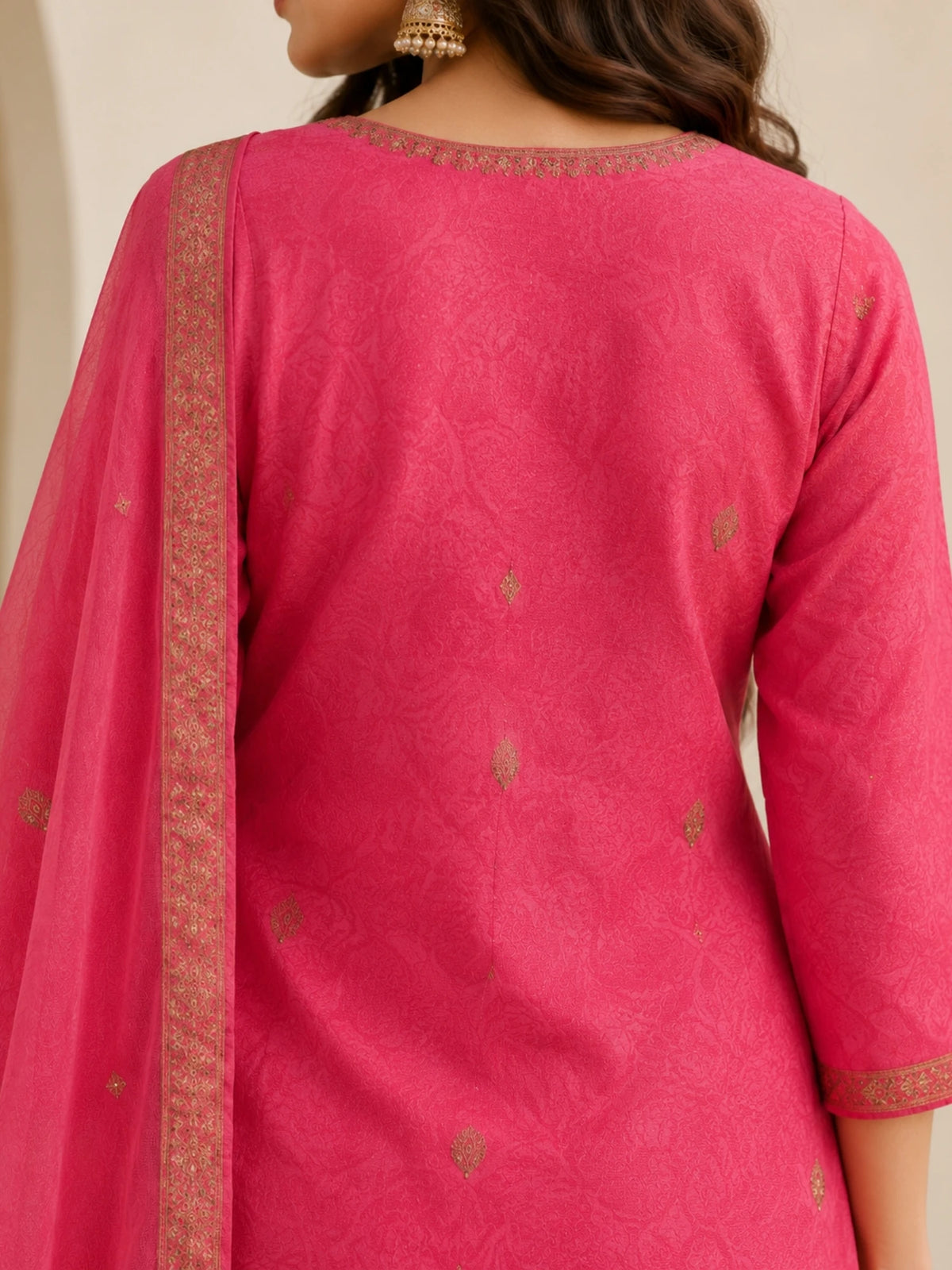 Woman wearing a pink embroidered suit with matching pants and a sheer dupatta indoors.