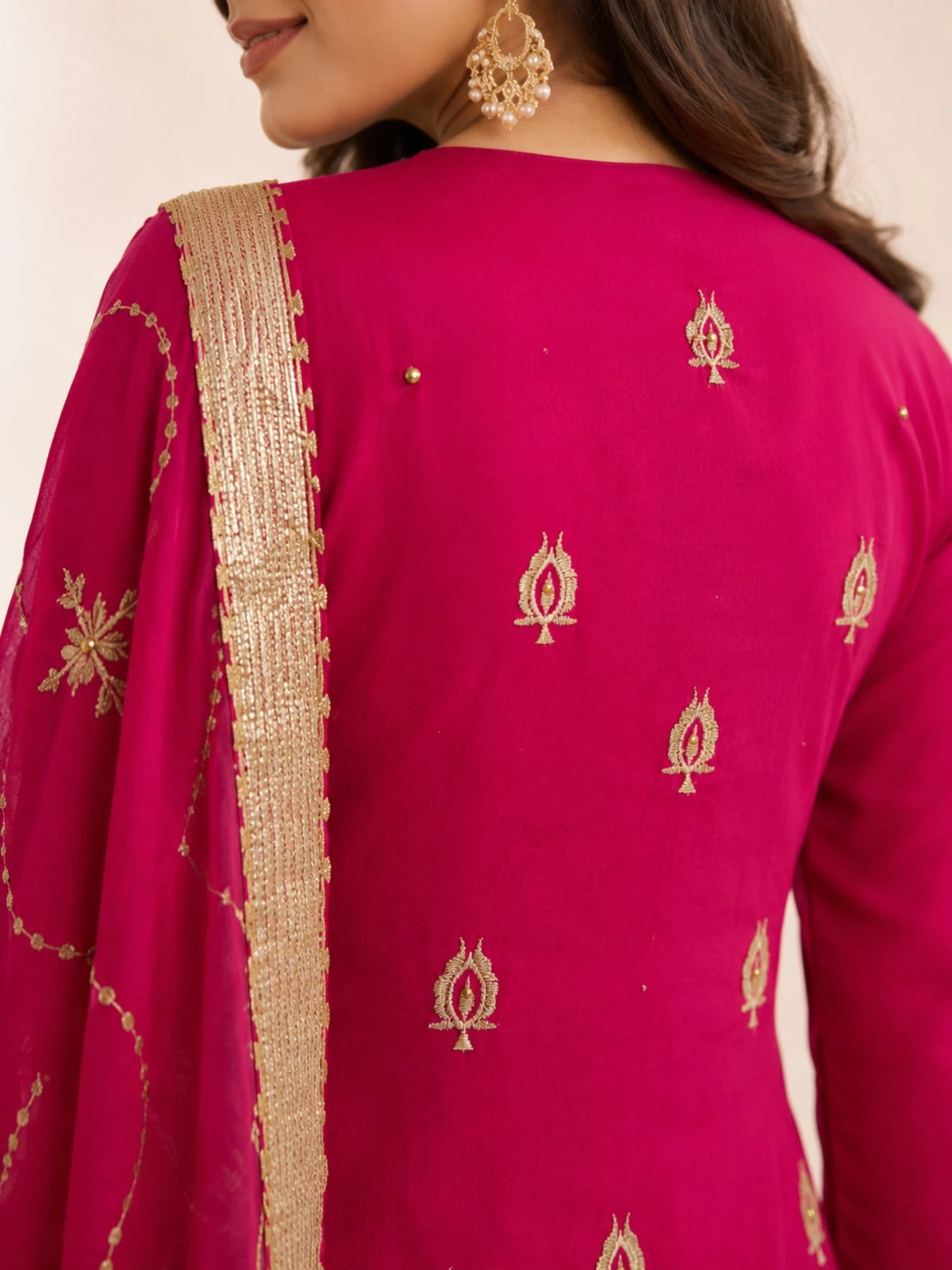 Woman wearing a pink embroidered suit with matching pants and a sheer dupatta indoors.