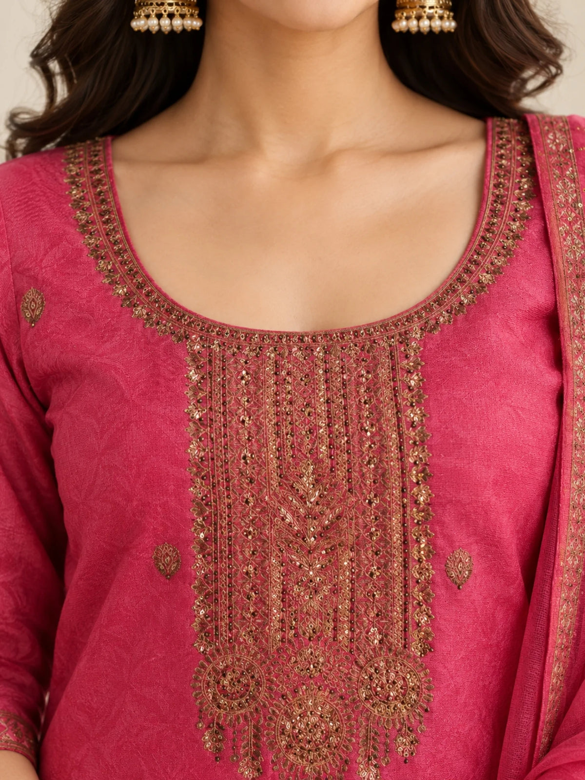 Woman wearing a pink embroidered suit with matching pants and a sheer dupatta indoors.