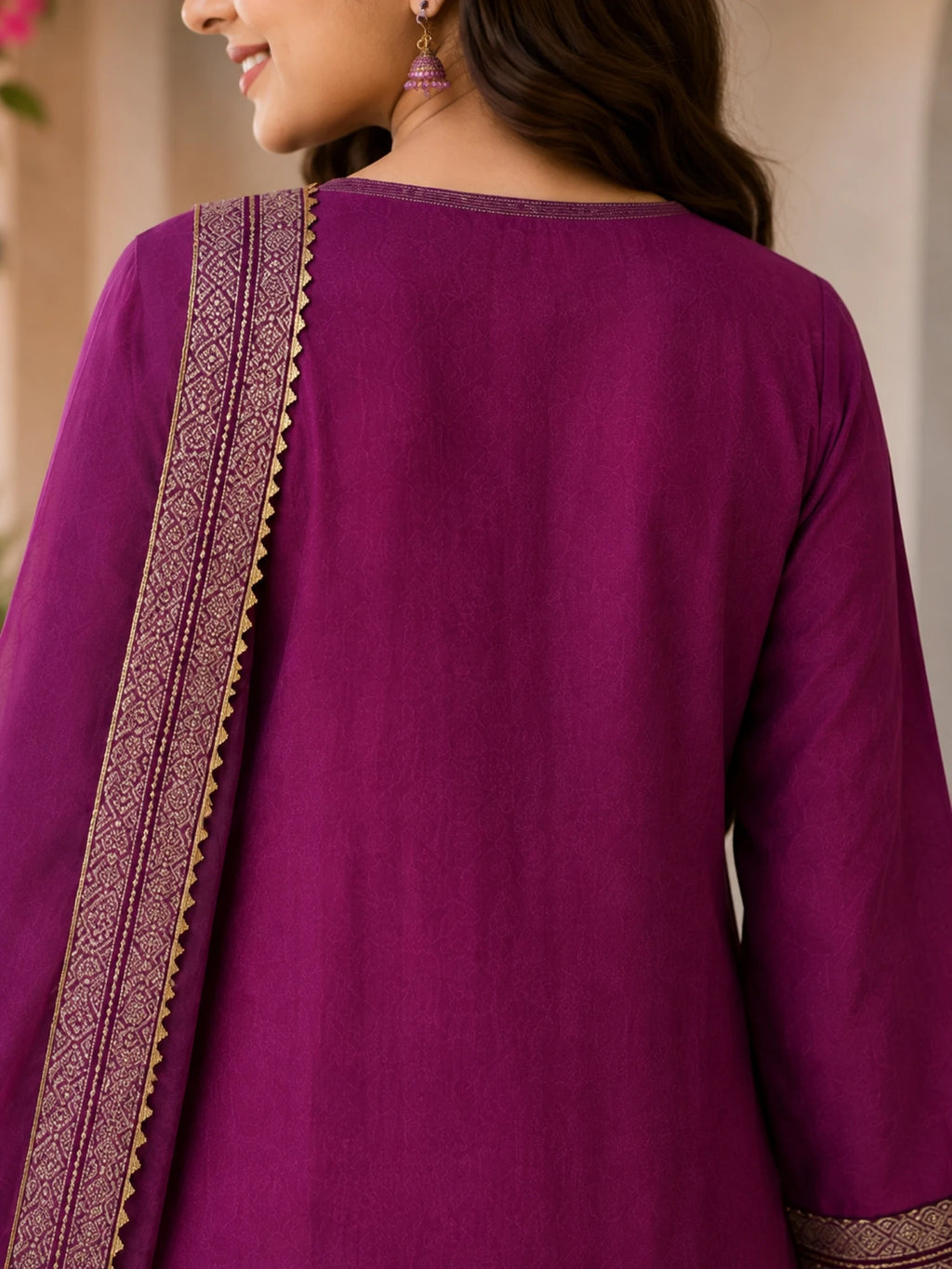 Woman wearing a plum purple suit with embellished borders and a matching dupatta outdoors.