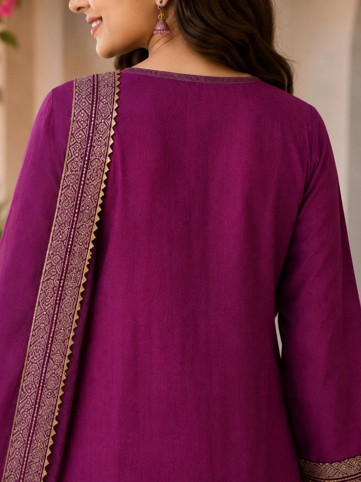 Woman wearing a plum purple suit with embellished borders and a matching dupatta outdoors.