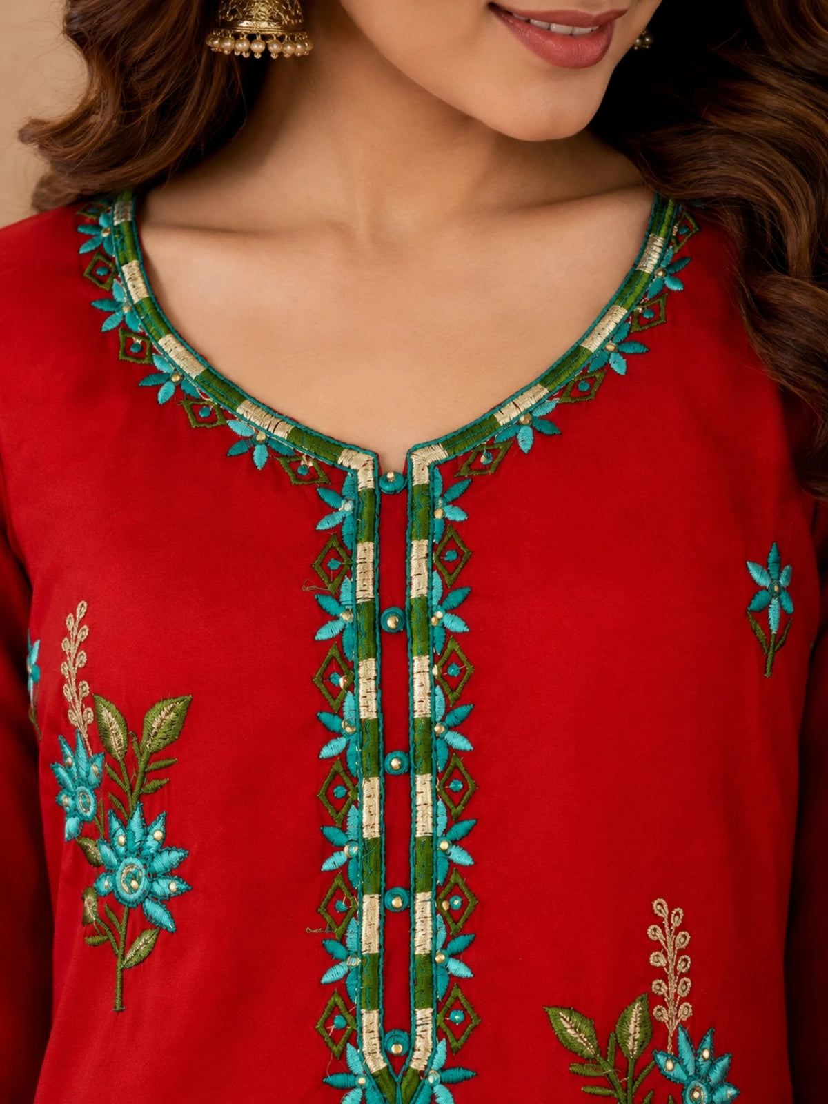 Red embroidered salwar suit with teal floral motifs and a sheer red dupatta with ornate borders.
