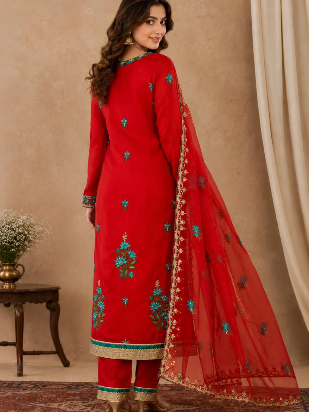 Red embroidered salwar suit with teal floral motifs and a sheer red dupatta with ornate borders.
