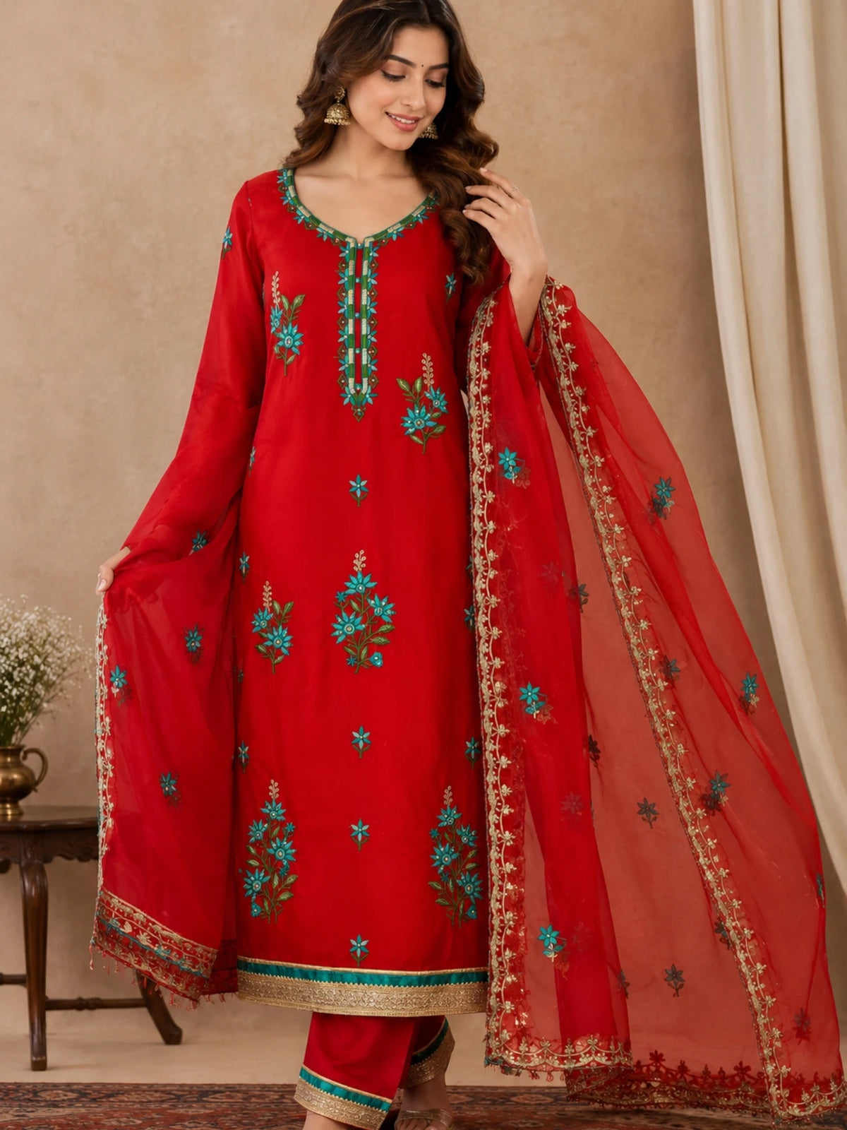 Red embroidered salwar suit with teal floral motifs and a sheer red dupatta with ornate borders.
