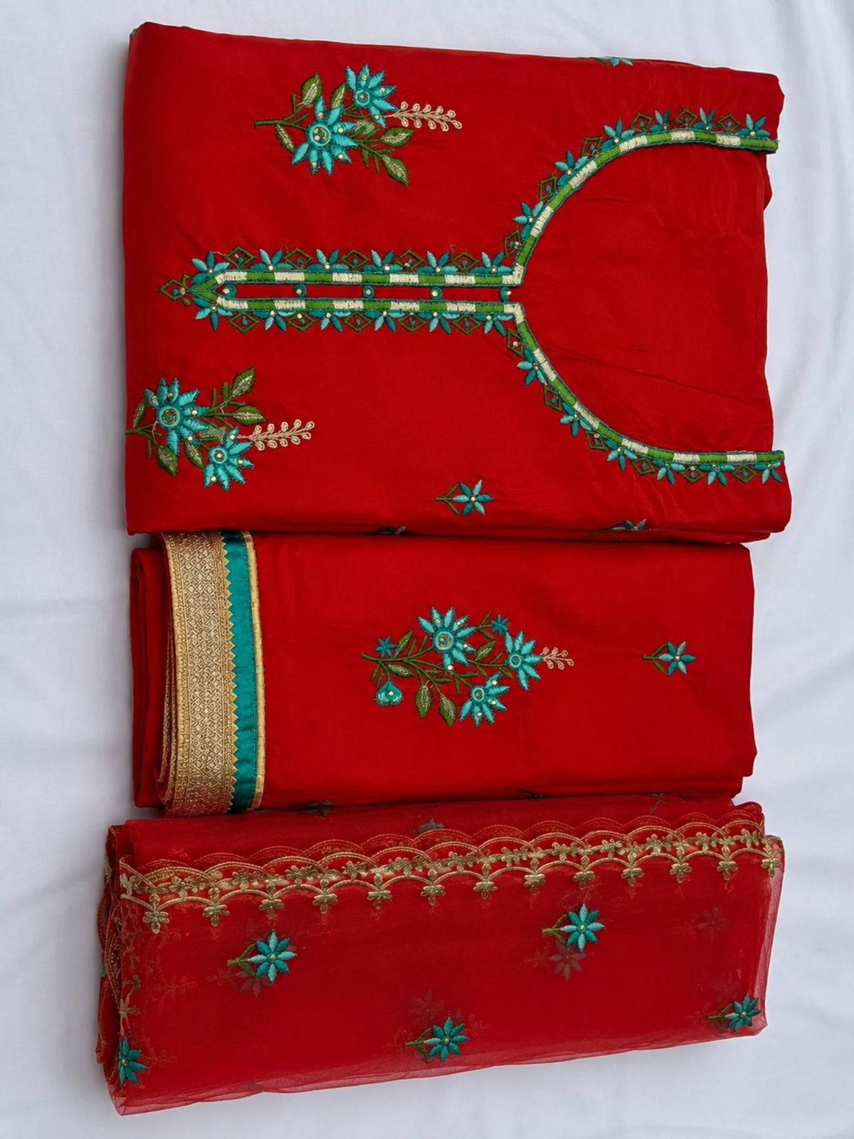 Red embroidered salwar suit with teal floral motifs and a sheer red dupatta with ornate borders.
