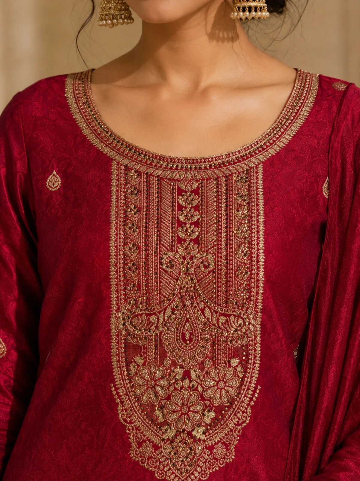 Woman wearing a deep red suit with gold embroidery, matching pants and an ornate dupatta.