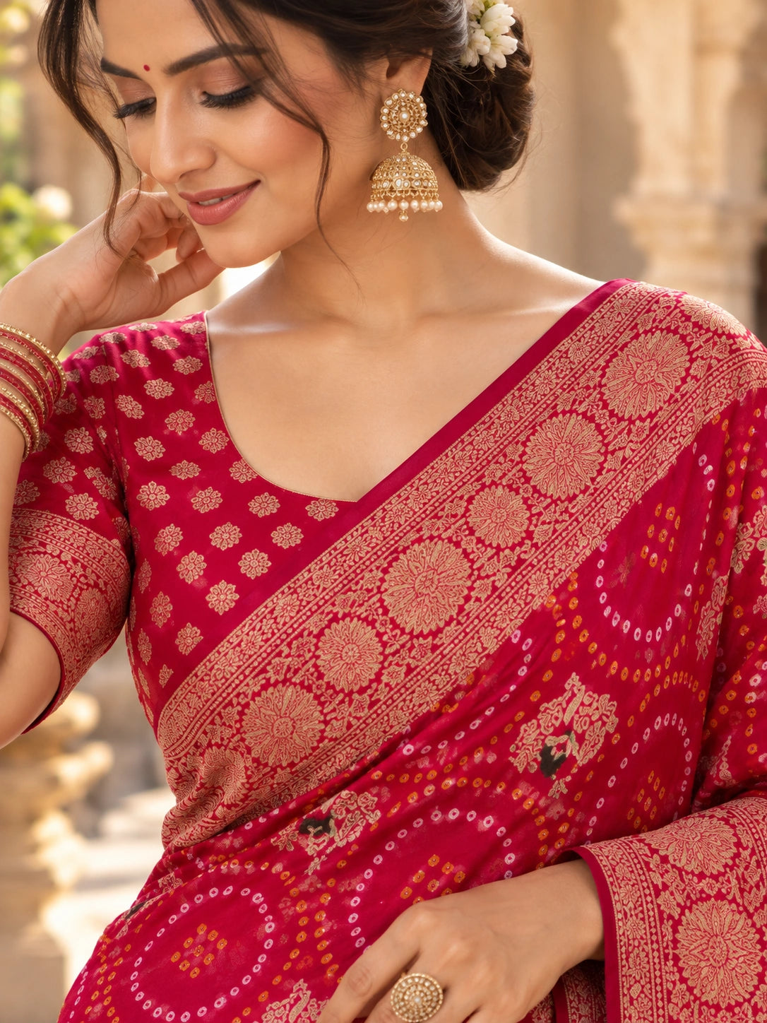 Red saree with gold floral motifs and an ornate border, draped on a woman in a traditional courtyard.
