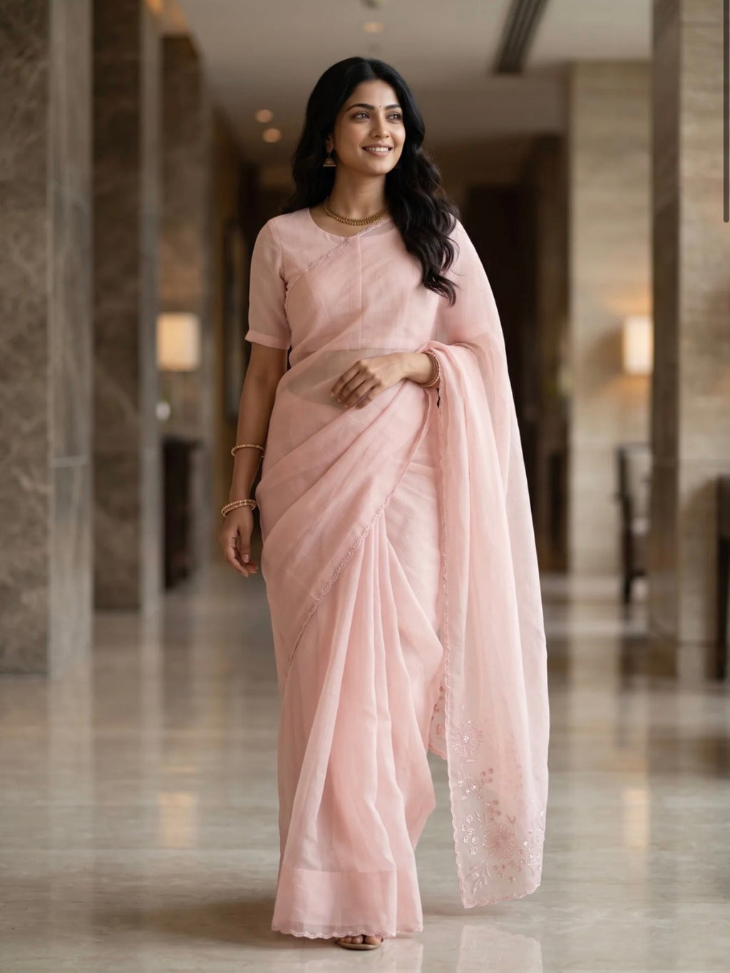Woman wearing a soft pink saree with a subtle border and matching blouse indoors.