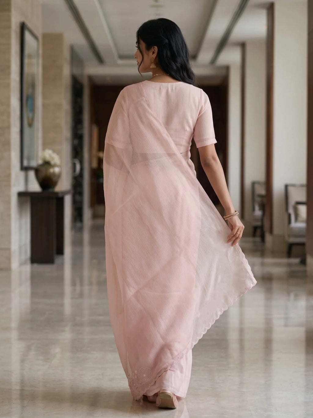 Woman wearing a soft pink saree with a subtle border and matching blouse indoors.