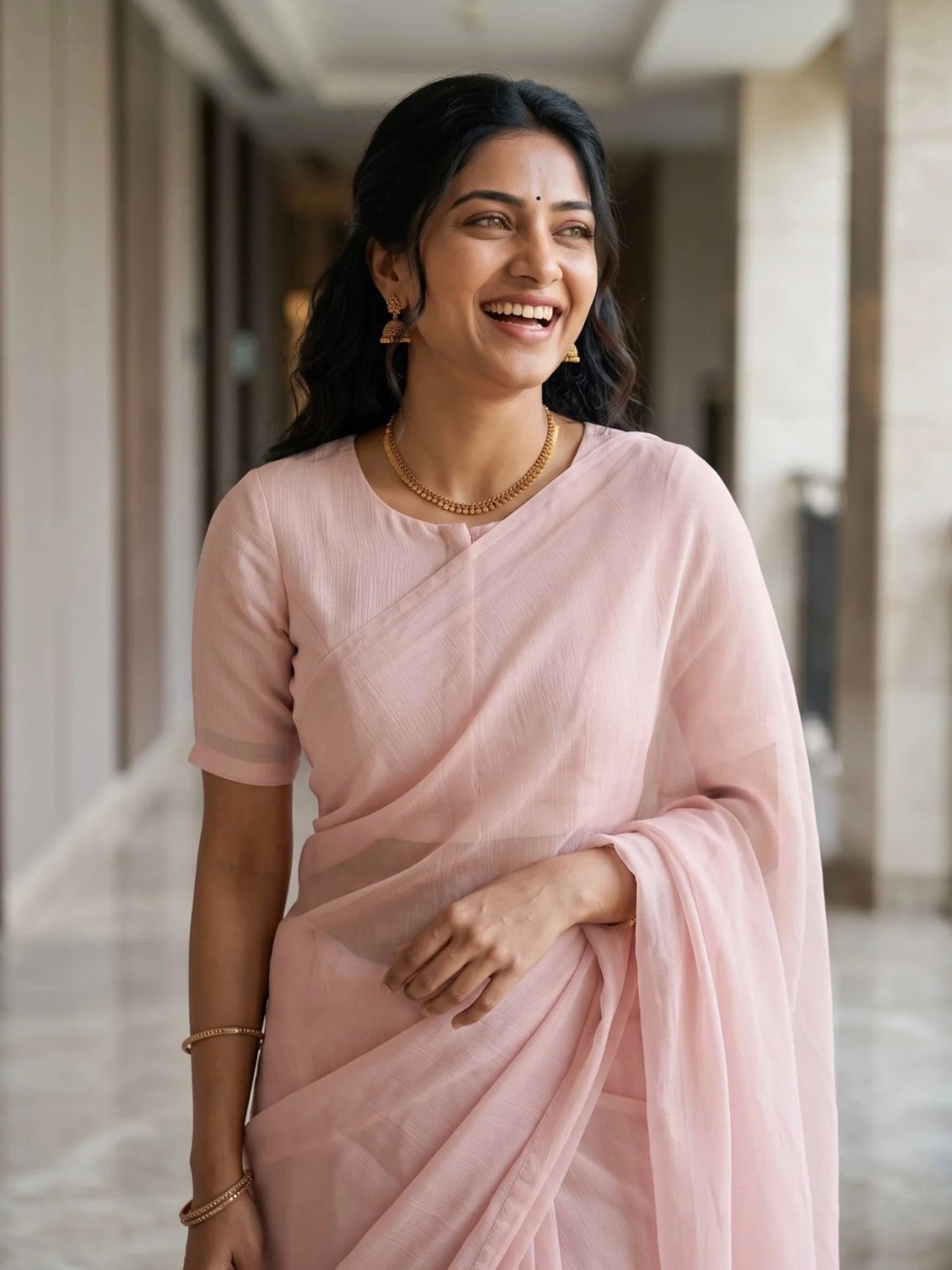 Woman wearing a soft pink saree with a subtle border and matching blouse indoors.