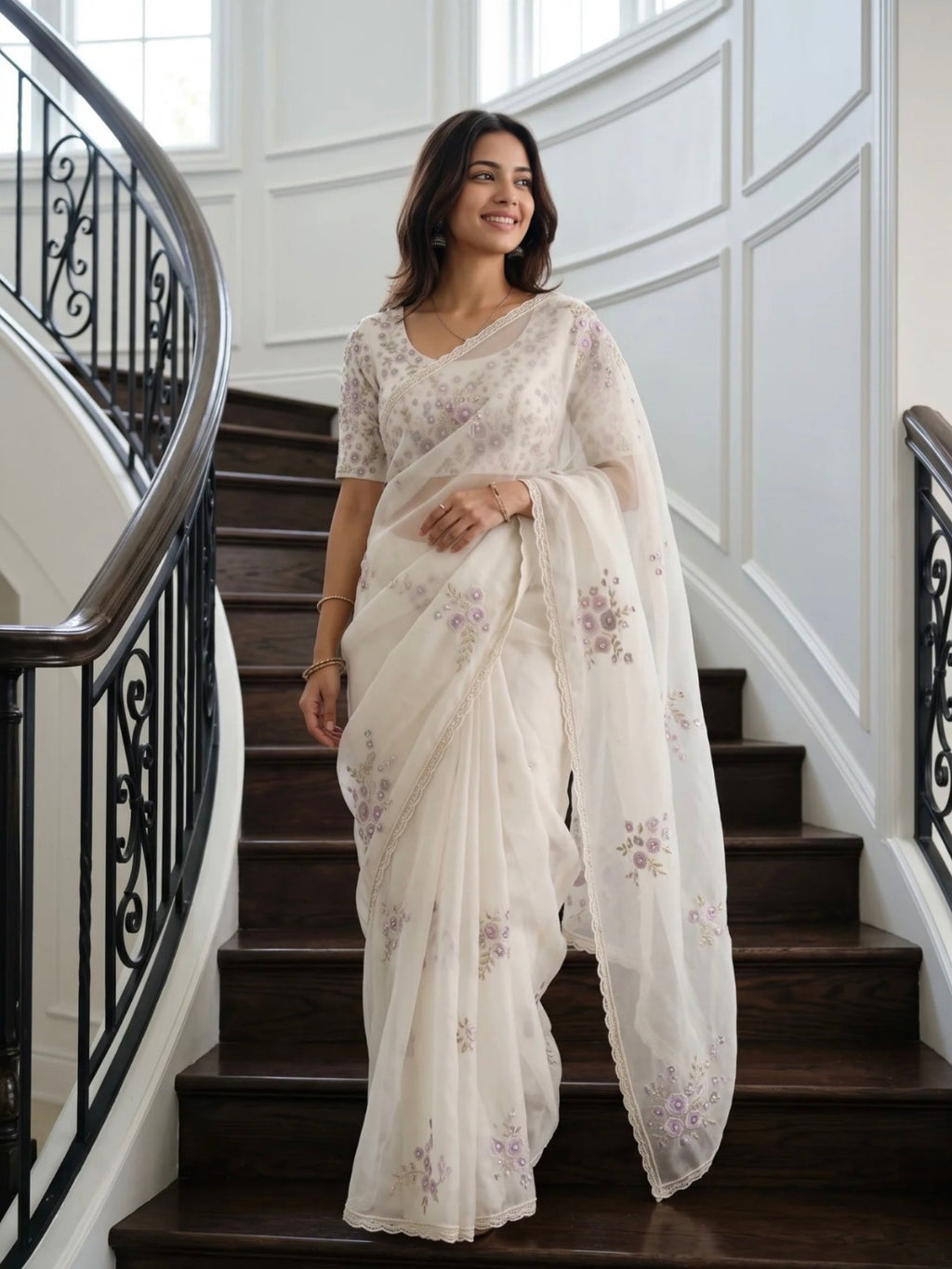 Woman wearing a white saree with lavender floral prints, standing on an elegant staircase.