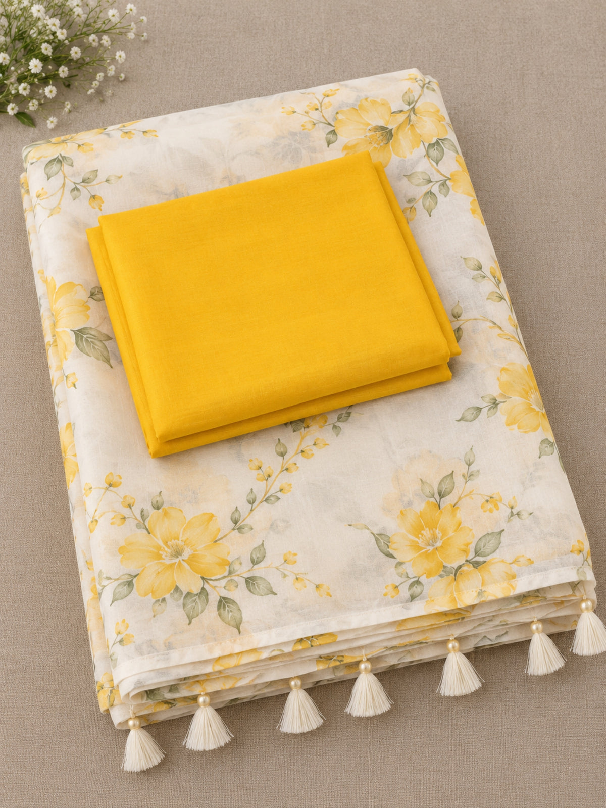 Woman wearing a white saree with yellow floral prints and tassel details indoors.