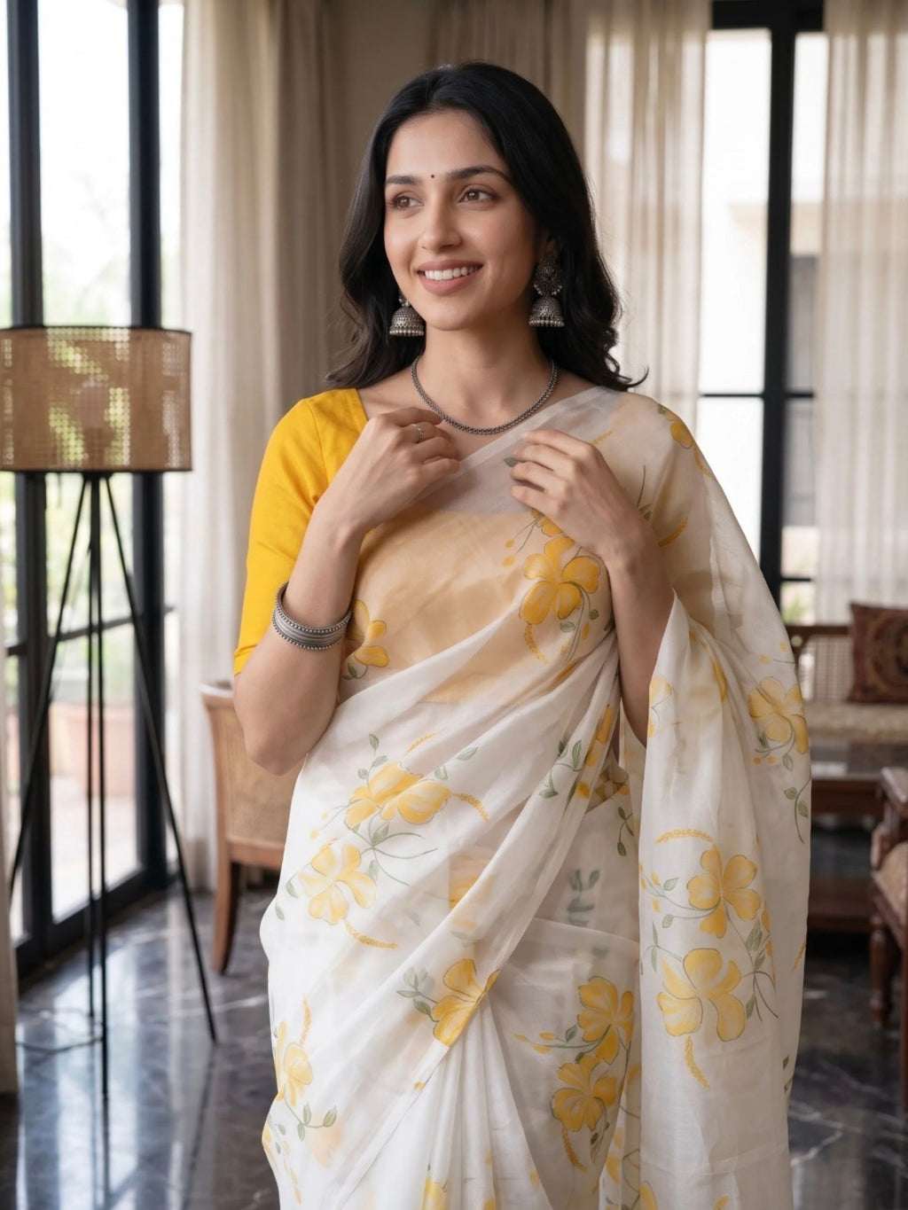 Woman wearing a white saree with yellow floral prints and tassel details indoors.