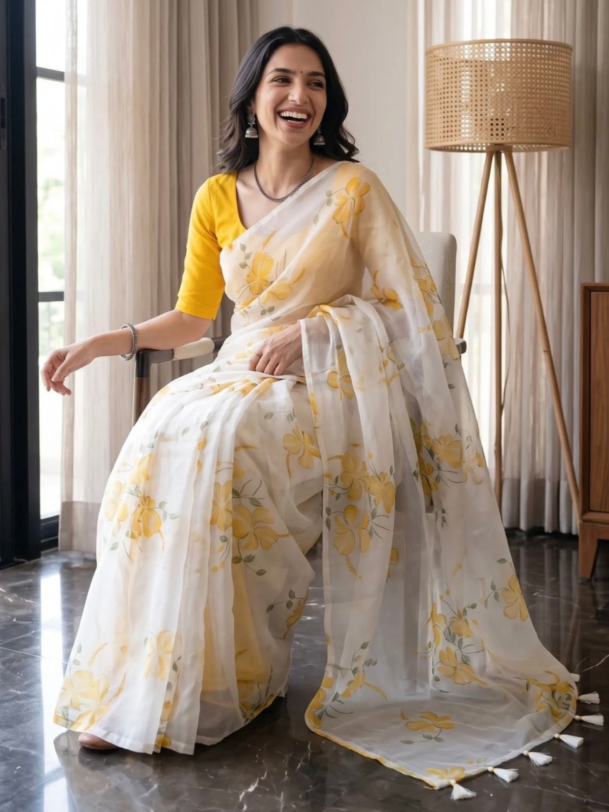 Woman wearing a white saree with yellow floral prints and tassel details indoors.