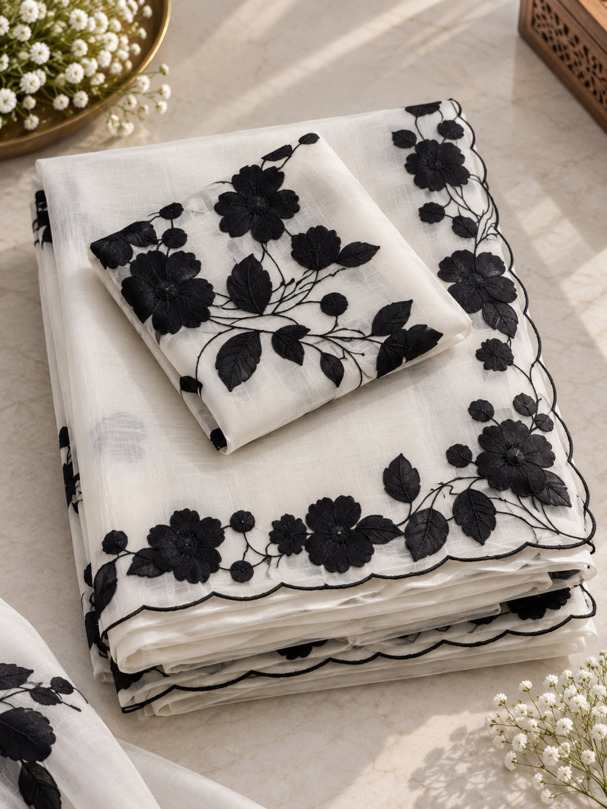 Woman wearing a white saree with black floral prints and a sheer pallu indoors.