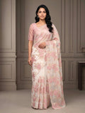 Woman wearing a white saree with pink floral embroidery and a matching pink blouse indoors.
